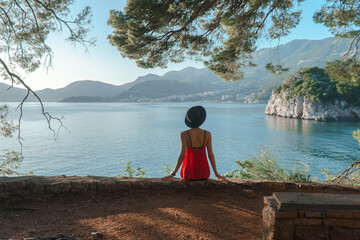 the girl sits on a cliff under an old tree with a beautiful view of the sea and mountains. Vacation in the European resort. Travel and leisure.