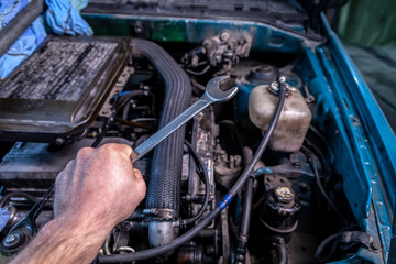 Fototapeta premium Close-up of a young car repairman holding a wrench in his hand and about to repair a car under the hood of a car. The concept of car repair and car repair shop