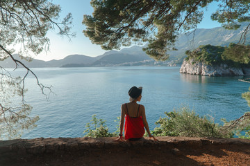 the girl sits on a cliff under an old tree with a beautiful view of the sea and mountains. Vacation in the European resort. Travel and leisure.