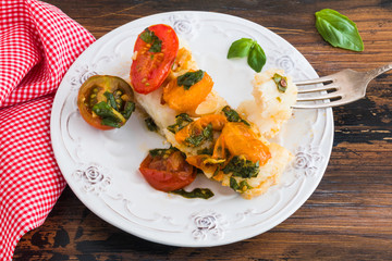 Baked cod fillet with cherry tomato and basil sauce on white plate on wooden rustic table