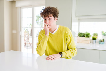 Young handsome man wearing yellow sweater at home looking stressed and nervous with hands on mouth biting nails. Anxiety problem.