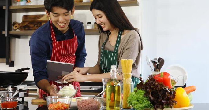 Lovely Asian couple cooking meal together, man finds recipe from teblet, they tease together, concept for lovely Asian couple in kitchen.