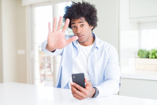 African American man using smartphone with open hand doing stop sign with serious and confident expression, defense gesture