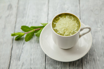 cup of hot matcha green tea latte and mint on grey wooden background