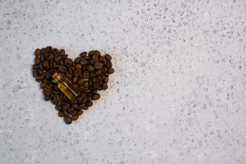 Coffee essential oil in a glass bottle, coffee beans in shape of heart on grey background