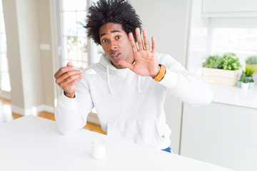 African American man eating healthy yogurt for breakfast with open hand doing stop sign with serious and confident expression, defense gesture