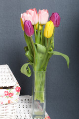 Bouquet of tulips of different colors on a gray background. Near wicker boxes.