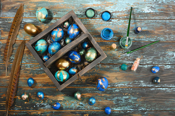 Painted colored Easter eggs in dark wooden box on dark wooden background. Boho stile.