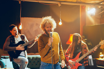 Band practicing for the gig.  Male singer with curly hair holding microphone and singing. In...