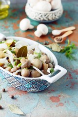 Delicious marinated mushrooms in a beautiful bowl with onions, pepper, dill and olive oil on a gray-blue background, top view, champignons
