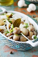 Delicious marinated mushrooms in a beautiful bowl with onions, pepper, dill and olive oil on a gray-blue background, top view, champignons
