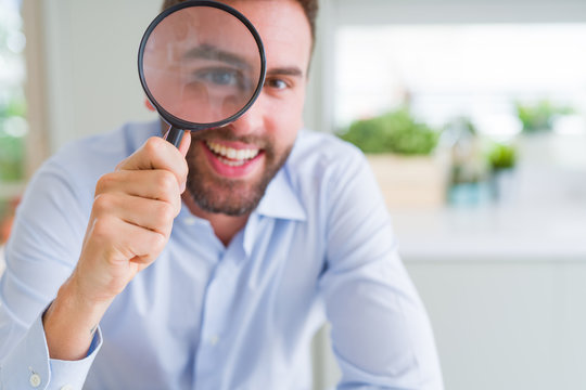 Handsome business man holding magnifying glass close to face, big eyes and funny expression