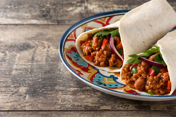 Typical Mexican burrito wrap with beef, frijoles and vegetables on wooden table. Copyspace