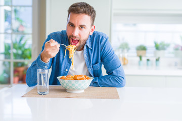 Handsome man eating pasta with meatballs and tomato sauce at home while smiling at the camera