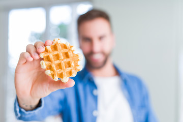 Obraz premium Handsome man eating sweet Belgian pancakes with a happy face standing and smiling with a confident smile showing teeth