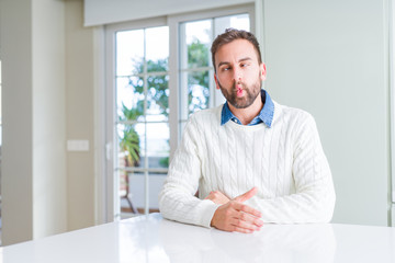 Fototapeta premium Handsome man wearing casual sweater making fish face with lips, crazy and comical gesture. Funny expression.