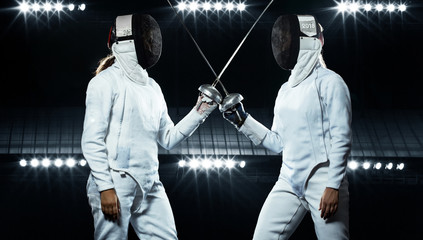 Young fencer athlete wearing mask and white fencing costume. holding the sword on black background with lights. - obrazy, fototapety, plakaty