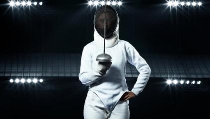 Young fencer athlete wearing fencing costume holding the sword and mask. Black background with...