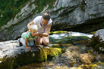 Mother with son drinking water from a pure, fresh and cool mountain stream on a family trip.