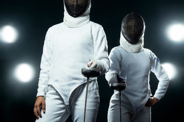 Young fencer athlete wearing mask and white fencing costume. holding the sword on black background...