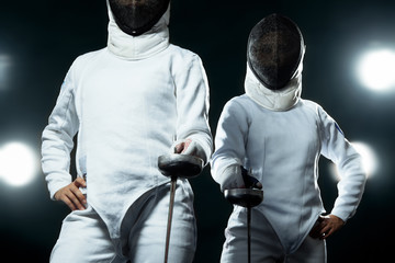 Young fencer athlete wearing mask and white fencing costume. holding the sword on black background...