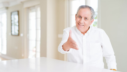 Fototapeta premium Handsome senior man at home smiling friendly offering handshake as greeting and welcoming. Successful business.