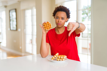 Young african american woman eating sweet waffle with angry face, negative sign showing dislike with thumbs down, rejection concept