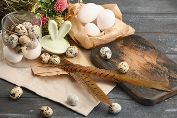 Open glass bowl with quail eggs, bunny ears, board, feathers and chiken eggs. Dyed wooden background. Eggs For Easter. Boho stile.
