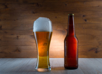 Glass of golden beer and bottle on wood background