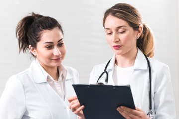 Two female assistants dressed in white coats talking to each other in the dentistry center