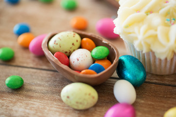Fototapeta na wymiar easter, food and holidays concept - close up of chocolate egg with candies and cupcake on wooden table