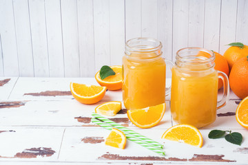 Orange juice in glass jars and fresh oranges on a white wooden rustic background.