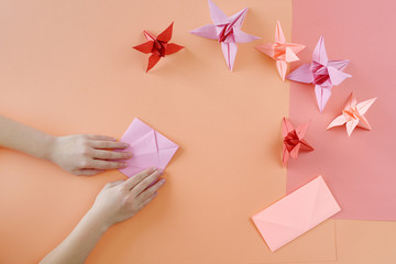 Children's hands do origami from colored paper on living coral background.