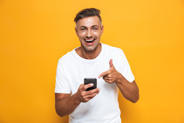 Happy man posing isolated over yellow wall background using mobile phone.