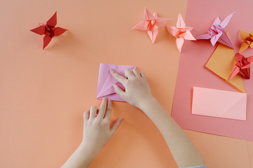 Children's hands do origami from colored paper on living coral background.