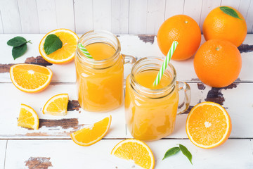 Orange juice in glass jars and fresh oranges on a white wooden rustic background.