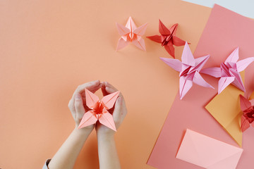 Children's hands do origami from colored paper on living coral background.