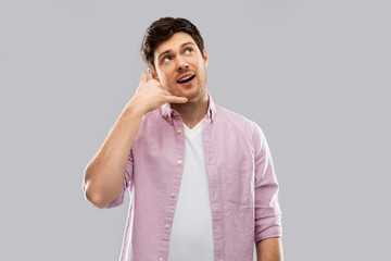 people concept - young man showing phone call gesture over grey background