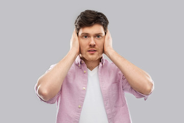 people, noise and stress concept - man closing ears by hands over grey background
