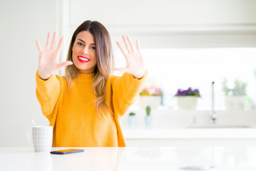 Young beautiful woman drinking a cup of coffee at home showing and pointing up with fingers number ten while smiling confident and happy.