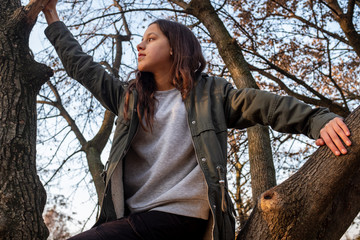 An attractive and thoughful teen girl standing between tree branches and looking away