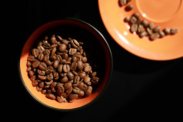 Orange cup with coffee beans on black background