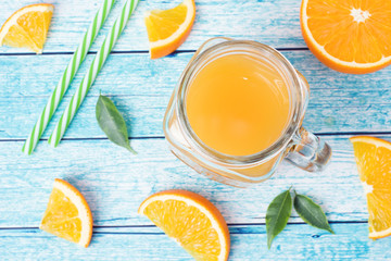 Orange juice in glass jars and fresh oranges on a blue background.