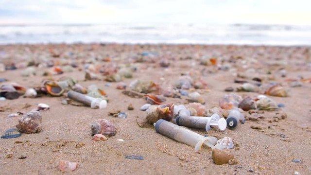 Medical syringes among the rapan shells in sand on sea beach after storm.