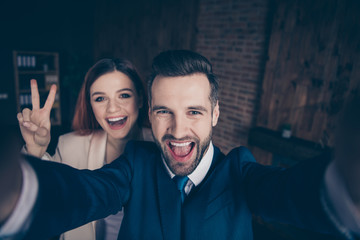 Close up photo she her business lady he him his guy laugh laughter hands arms hold smart phone telephone make take selfies show v-sign say hi crazy  stand office wearing formal wear suits