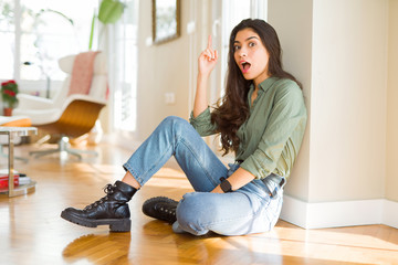 Young beautiful woman sitting on the floor at home pointing finger up with successful idea. Exited and happy. Number one.