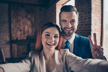 Close up photo she her pretty business lady he him his handsome guy laugh laughter hands arms hold smart phone make take selfies show v-sign say hi stand office wearing formal wear suits