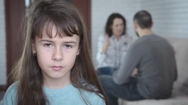 Family problems. Portrait of a sad little girl against the background of parents quarreling with each other.