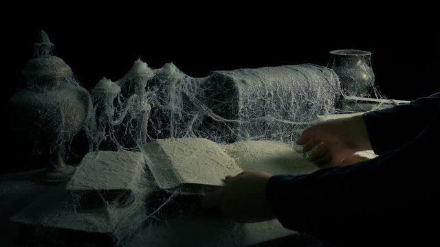 Person Picks Up Book From Under Cobwebs