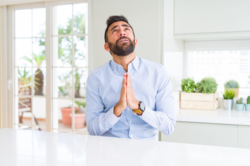 Handsome hispanic business man begging and praying with hands together with hope expression on face...